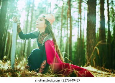 Divine Female Warrior Valkyrie Holds A Sword In Her Hand In A Forest Lit By Sunlight. Scandinavian Mythology. Epic Fantasy.