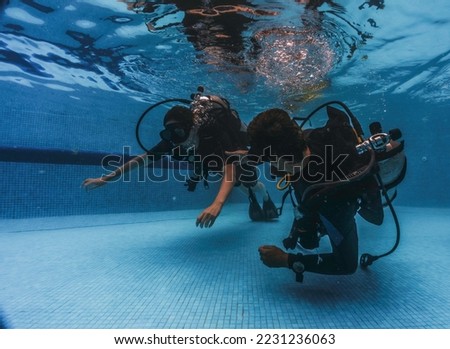 diving instructor teaches students to scuba dive in swimming pool. couple getting first experience with scuba diving under the guidance of experienced recreational diving instructor on vacation.