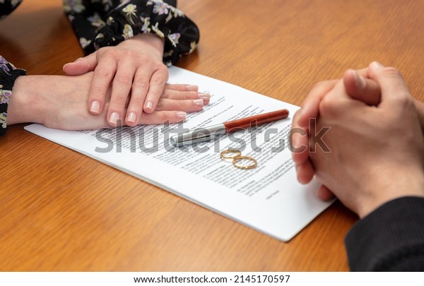 Divorce agreement, marriage dissolution\
documents. Man and woman hands, wedding rings and legal papers for\
signature on a wooden table, lawyer\
office