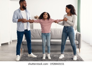 Divorce Concept. Portrait of angry African American parents fighting over their child, mad man and woman quarrelling, pulling daughter's hands in different directions. Domestic Violence, Separation