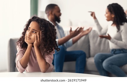 Divorcio Y Violencia Doméstica. Retrato de la hija afroamericana molesta que mira a través de la ventana mientras sus padres enojados que luchan en el fondo, niño deprimido que se siente solo