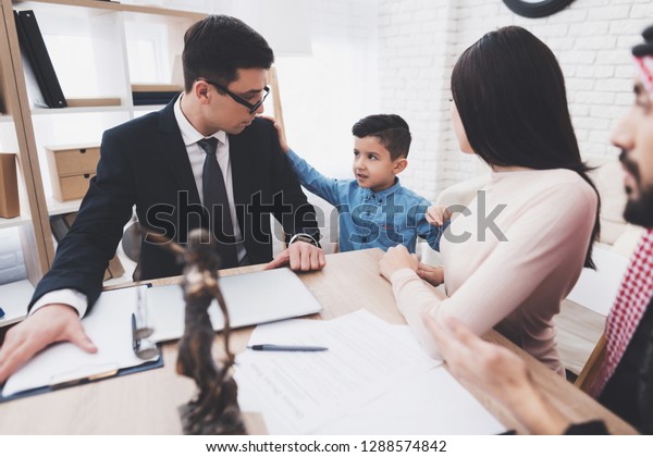 Divorce lawyer in suit in office with\
arab husband and wife. Son is choosing\
mother.