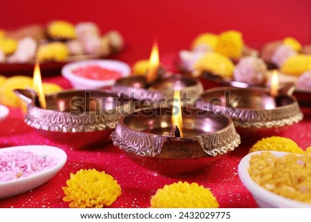 Diwali celebration. Diya lamps, bright rangoli and chrysanthemum flowers on shiny red table, closeup