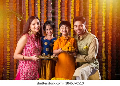 Diwali Or Rakshabandhan Celebration - Indian Young Family Of Four Celebrating Deepavali Or Bhai Dooj Festival With Sweet Laddoo, Oil Lamp Or Diya And Gift Boxes, Eating Food Or Taking Selfie