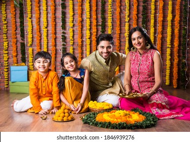 Diwali Or Rakshabandhan Celebration - Indian Young Family Of Four Celebrating Deepavali Or Bhai Dooj Festival With Sweet Laddoo, Oil Lamp Or Diya And Gift Boxes, Eating Food Or Taking Selfie