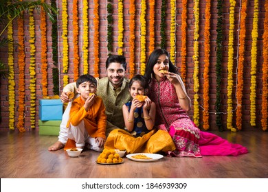 Diwali Or Rakshabandhan Celebration - Indian Young Family Of Four Celebrating Deepavali Or Bhai Dooj Festival With Sweet Laddoo, Oil Lamp Or Diya And Gift Boxes, Eating Food Or Taking Selfie