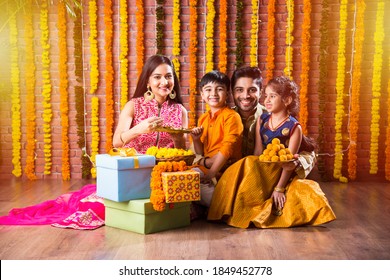 Diwali Or Rakshabandhan Celebration - Indian Young Family Of Four Celebrating Deepavali Or Bhai Dooj Festival With Sweet Laddoo, Oil Lamp Or Diya And Gift Boxes, Eating Food Or Taking Selfie