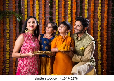 Diwali Or Rakshabandhan Celebration - Indian Young Family Of Four Celebrating Deepavali Or Bhai Dooj Festival With Sweet Laddoo, Oil Lamp Or Diya And Gift Boxes, Eating Food Or Taking Selfie