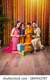 Diwali Or Rakshabandhan Celebration - Indian Young Family Of Four Celebrating Deepavali Or Bhai Dooj Festival With Sweet Laddoo, Oil Lamp Or Diya And Gift Boxes, Eating Food Or Taking Selfie