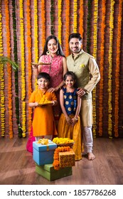 Diwali Or Rakshabandhan Celebration - Indian Young Family Of Four Celebrating Deepavali Or Bhai Dooj Festival With Sweet Laddoo, Oil Lamp Or Diya And Gift Boxes, Eating Food Or Taking Selfie