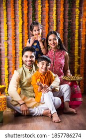 Diwali Or Rakshabandhan Celebration - Indian Young Family Of Four Celebrating Deepavali Or Bhai Dooj Festival With Sweet Laddoo, Oil Lamp Or Diya And Gift Boxes, Eating Food Or Taking Selfie