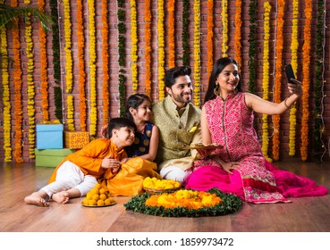 Diwali Or Rakshabandhan Celebration - Indian Young Family Of Four Celebrating Deepavali Or Bhai Dooj Festival With Sweet Laddoo, Oil Lamp Or Diya And Gift Boxes, Eating Food Or Taking Selfie