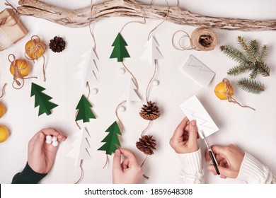 DIY Christmas Home Decor From Natural Materials. Hands Make Garland Of Paper Trees, Twine And Cones.