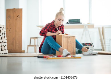 DIY concept. Young woman repairing furniture at home, sitting on the floor. - Powered by Shutterstock