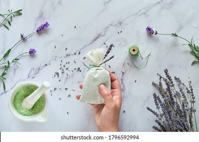 DIY Handmade Lavender Sachets And Sugar Scrub. Hand Holds Linen Bag With Dry Lavender Flowers. Flat Lay, Top View On White Marble Background.