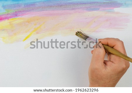 DIY, learning to draw, hobbies. Paint a picture on paper. Step 2: Picture the sunlight. A woman's hand Brushes yellow paint on top of a sheet of paper.