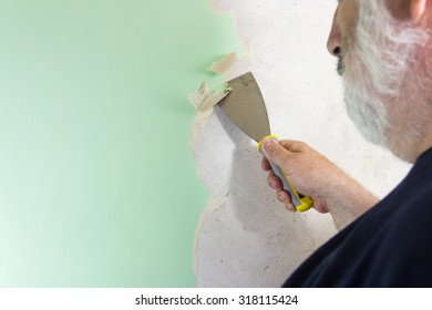 DIY Man Wallpaper Stripping. Using A Stripping Tool To Remove Old Wallpaper From An Old Domestic Interior Wall. 