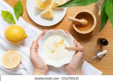 DIY Natural Face Mask Ingredients For Bright And Healthy Skin. Woman Hand Holding A Bowl Of Homemade Face Mask W/ Yogurt, Lemon, Honey And Essential Oil On Wood Table. Beauty Herbal Skin Care Concept.