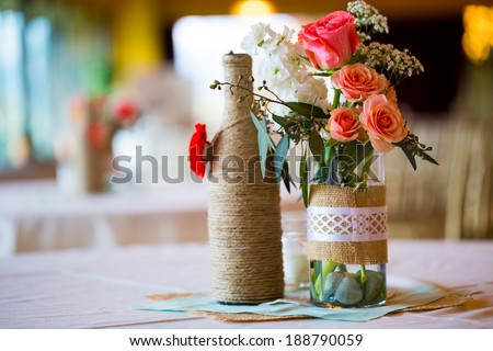 DIY wedding decor table centerpieces with wine bottles wrapped in burlap twine and rose flowers.