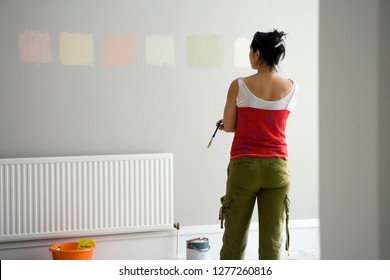 DIY woman choosing paint color swatches on room wall deciding on decor for home improvement