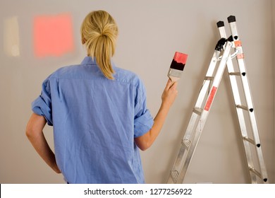 Diy Woman Decorating At Home Painting Wall With Test Swatches Holding Paintbrush Dipped In Red Paint