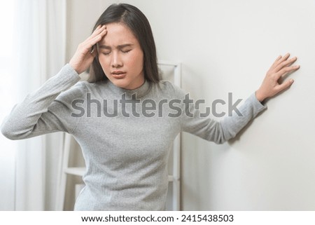 Dizzy asian young woman, girl headache or migraine pain. suffering from vertigo, difficulty standing up leaning on wall at home, holding head with hand, health problem of brain, inner ear not balance.