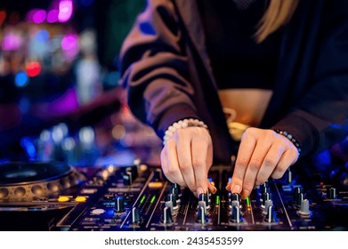 A DJ deftly adjusts knobs on a vibrant console, immersed in the pulsating rhythm of the nightlife. Colorful lights illuminate the scene, creating an electric atmosphere - Powered by Shutterstock