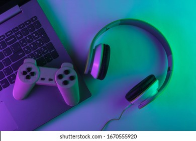 DJ or gaming concept. Laptop, headphones and gamepad with neon green purple light. Gradient glow. Top view - Powered by Shutterstock