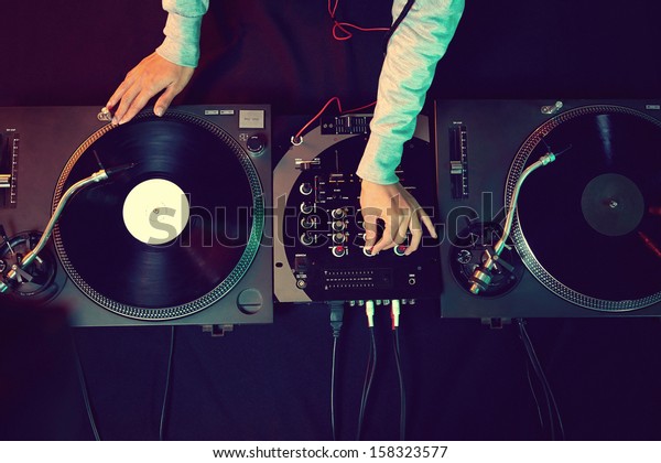 Dj hands on equipment deck and mixer with vinyl\
record at party
