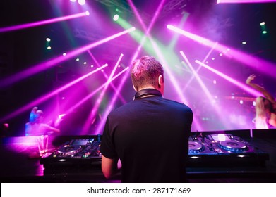 DJ With Headphones At Night Club Party Under The Blue Light And People Crowd In Background
