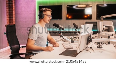The DJ hosts the program and communicates with the audience on air at the radio station. The announcer reads the news. A male radio host speaks into a microphone and records a podcast