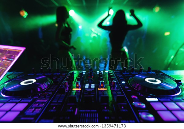 DJ mixer controller in a\
nightclub with dancing on the background of go-go dance girls at a\
party