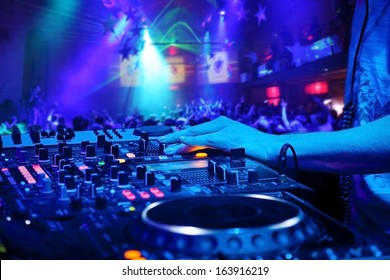 Dj mixes the track in the nightclub at party.  On background of people dancing and a laser show