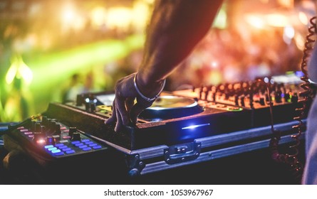 Dj mixing outdoor at beach party festival with crowd of people in background - Summer nightlife view of disco club outside - Soft focus on hand fingers - Fun ,youth,entertainment and fest concept