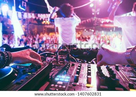 Dj mixing outdoor at beach party festival outdoor with crowd of people in background - Soft focus on left hand - Fun, summer, youth, nightlife, music, nightclubs and entertainment concept