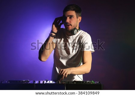 DJ playing music at mixer on color foggy background