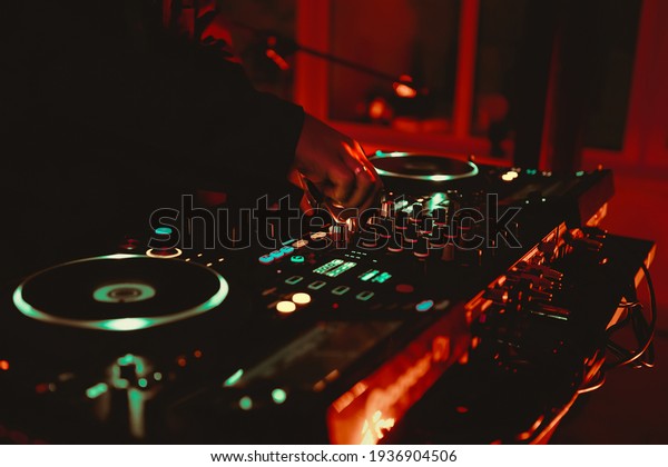 Dj playing music on rave party in nightclub.\
Professional disc jockey plays concert turntables,sound mixer\
devices on stage in dark night club.Royalty free curated collection\
with parties and concerts