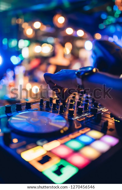 DJ plays live set and mixing music on turntable\
console at stage in the night club. Disc Jokey Hands on a sound\
mixer station at club party. DJ mixer controller panel for playing\
music and partying.