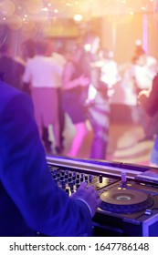 DJ plays music from CDs and dancing people in the background during party event or wedding celebration