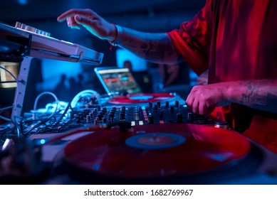 The DJ in the red T-shirt plays on the DJ equipment, play vinyl turntable, on the microbrand console using the controller. disco DJ. night life. atmosphere. club photo