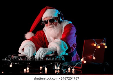 DJ Santa Claus mixing tracks in a nightclub at a Christmas and New Year party or Corporate events. Senior disc jockey as Santa listening music, headphones, laptop, mixer controller player, turntable. - Powered by Shutterstock