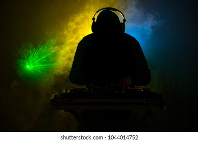 DJ Spinning, Mixing, and Scratching in a Night Club, Hands of dj tweak various track controls on dj's deck, strobe lights and fog, or Dj mixes the track in the nightclub at party. Selective focus - Shutterstock ID 1044014752