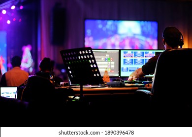 DJ technician engineer operating stage light live broadcast audio video equipment control center in computer monitors to switch camera scenes, music, sound, and lighting effects in holiday event show.