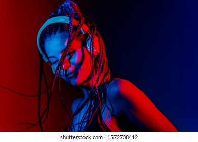 Dj woman with tree braids, dancing with headphones and with a smiling expression. With blue and red color lights.