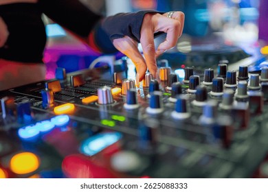 A DJ's hand adjusting knobs on a professional audio mixer in a vibrant club setting, highlighting the dynamic and engaging atmosphere of live music mixing.