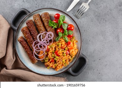 Djuvec rice cooked with red bell pepper, tomato, peas, paprik and beef cevapcici. Grey background, copy space.
