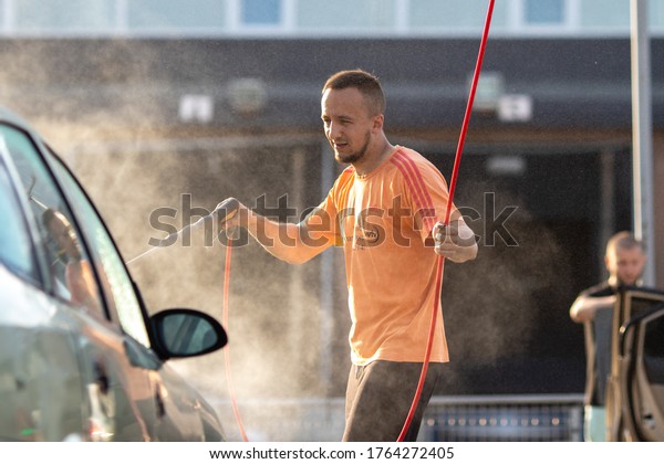 \
DNEPRO,\
UKRAINE - June 20, 2020. A dark-haired man with a dark brown skin\
and middle-aged skin in a red T-shirt with a small beard washes a\
car in a car wash. With blurry\
background.