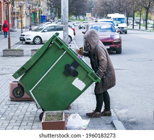 Dnepropetrovsk, Ukraine - 04.21.2021: Poor Hungry Woman Looking For Food In A Trash Can On The Street. The Homeless Person Has No Money Or Housing