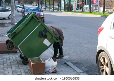 Dnepropetrovsk, Ukraine - 04.21.2021: Poor Hungry Woman Looking For Food In A Trash Can On The Street. The Homeless Person Has No Money Or Housing