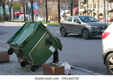 Dnepropetrovsk, Ukraine - 04.21.2021: Poor Hungry Woman Looking For Food In A Trash Can On The Street. The Homeless Person Has No Money Or Housing